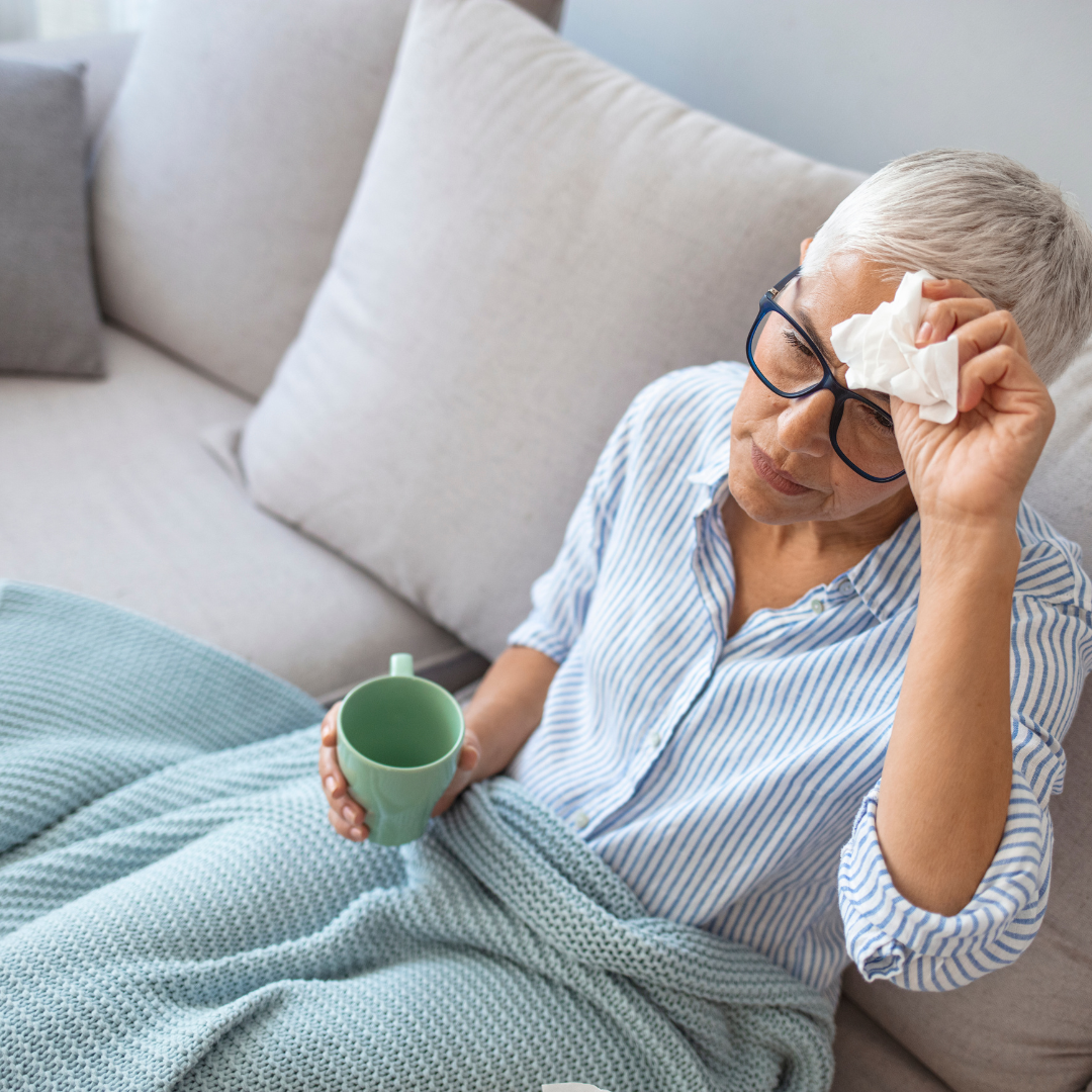 Elderly woman holding head with a tissue in one hand and mug in the other.